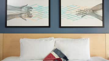 Een bed met wit beddengoed en twee kussens, één effen en één met een rood-blauwe print.