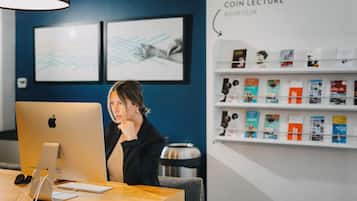 Una mujer sentada en un escritorio con un iMac de Apple, auriculares y un teclado. En la pared hay obras de arte enmarcadas y una estantería llena de libros.