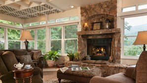 A cozy living room with a stone fireplace, comfortable seating, and large windows offering a view of greenery. - Andon-Reid Inn B&B (Waynesville)