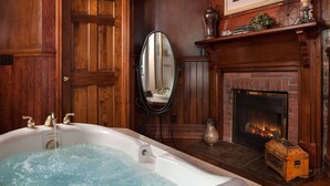 A bathroom with a bathtub, a mirror, a fireplace, and wooden paneling. - Andon-Reid Inn B&B (Waynesville)