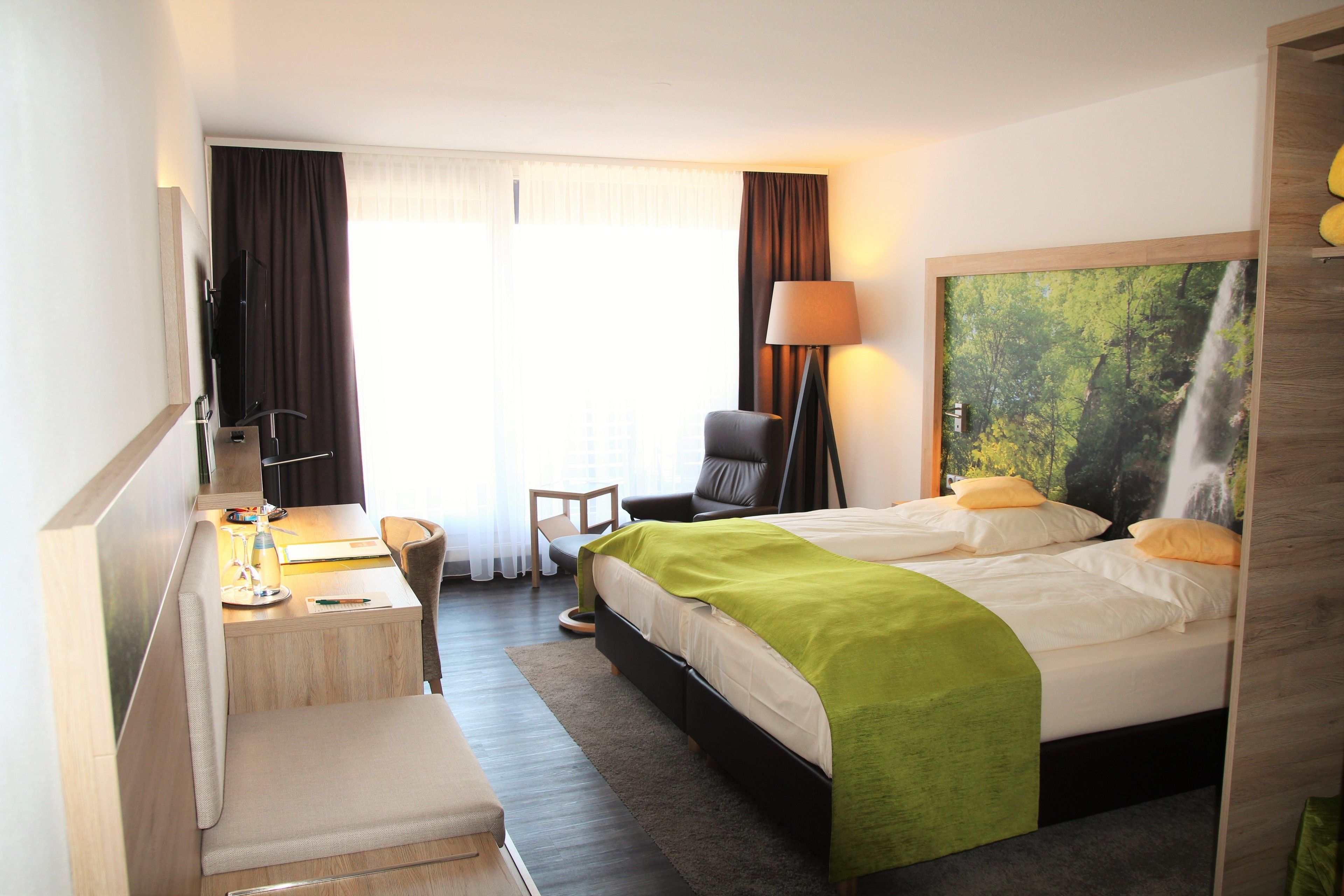 Habitación de hotel con cama, escritorio, silla y una ventana grande con cortinas.