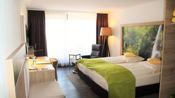 Habitación de hotel con cama, escritorio, silla y una ventana grande con cortinas.