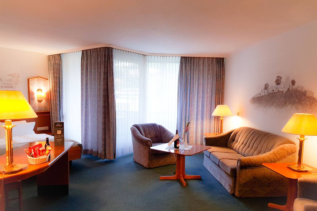Habitación de hotel con cama, escritorio, dos sillas, un sofá y un ventanal con cortinas.