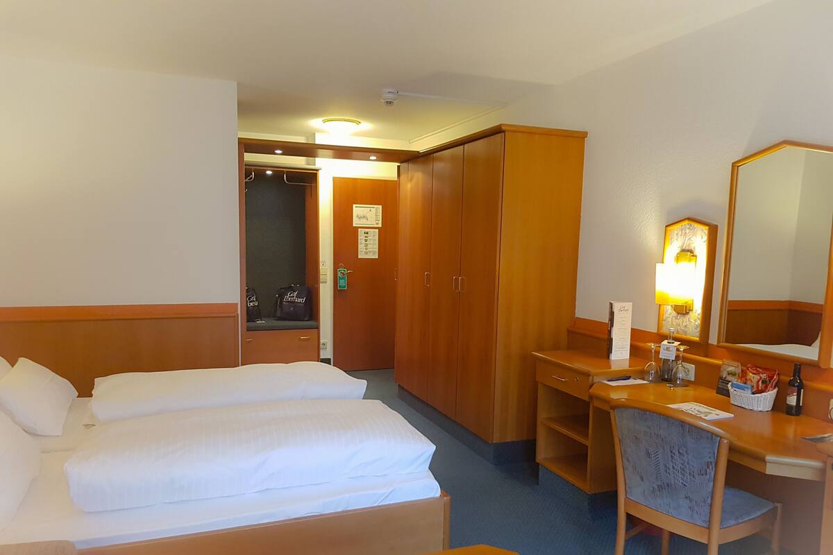 Habitación de hotel con cama, escritorio, silla, armario y espejo.