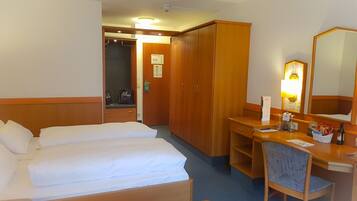 A hotel room with a bed, a desk, a chair, a wardrobe, and a mirror.