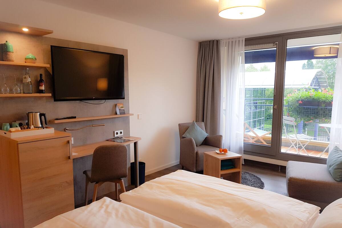 Habitación de hotel con cama, escritorio, silla, televisor y ventana con vista al exterior.