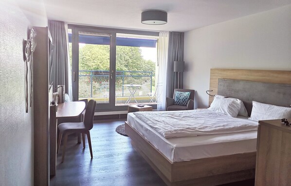 Une chambre d’hôtel comprenant un lit, un bureau, une chaise, une petite table et un balcon avec vue sur la verdure.
