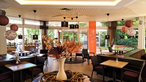 A restaurant with wooden furniture, large windows, and decorative plants.