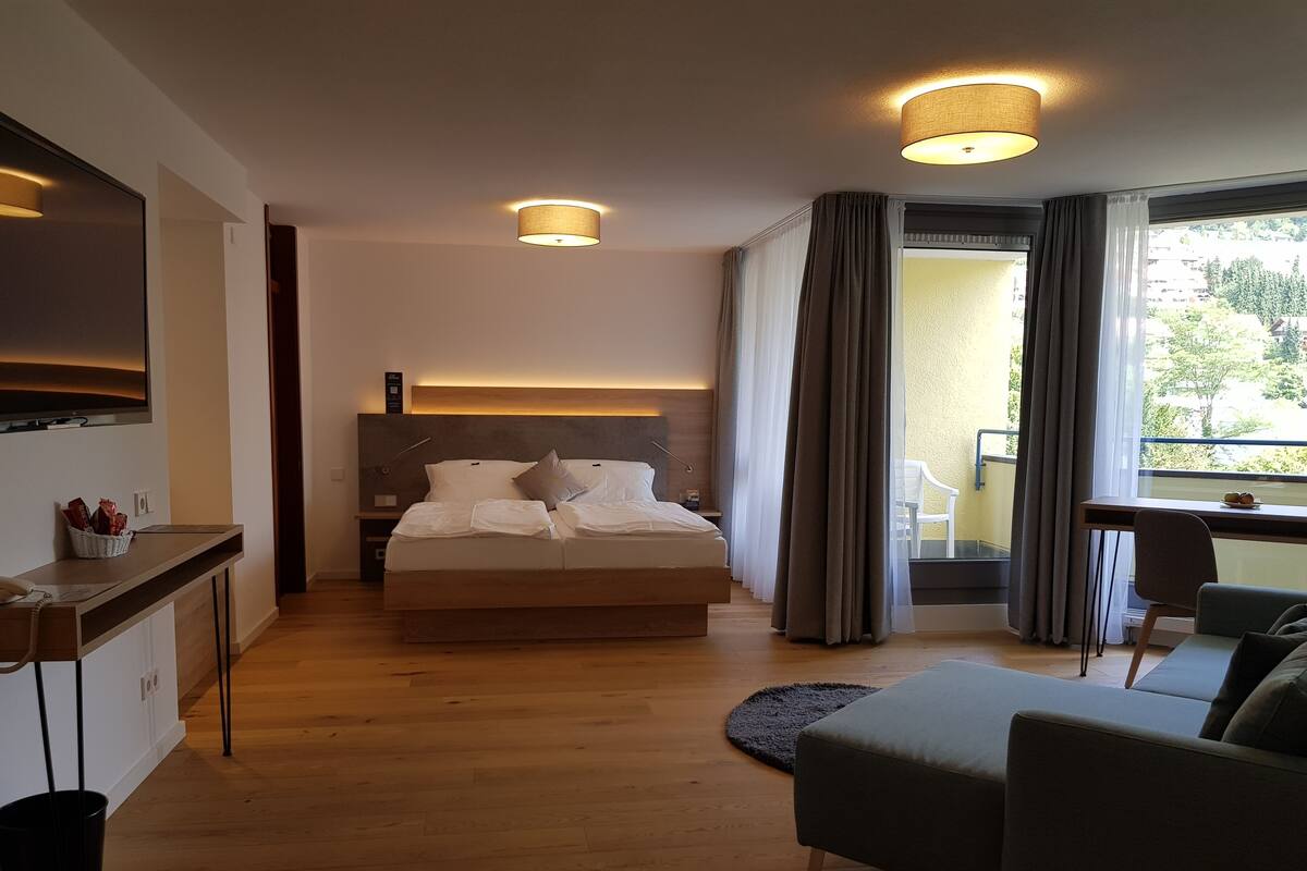 Una habitación de hotel moderna con una cama grande, un escritorio, un sofá y un balcón con cortinas.
