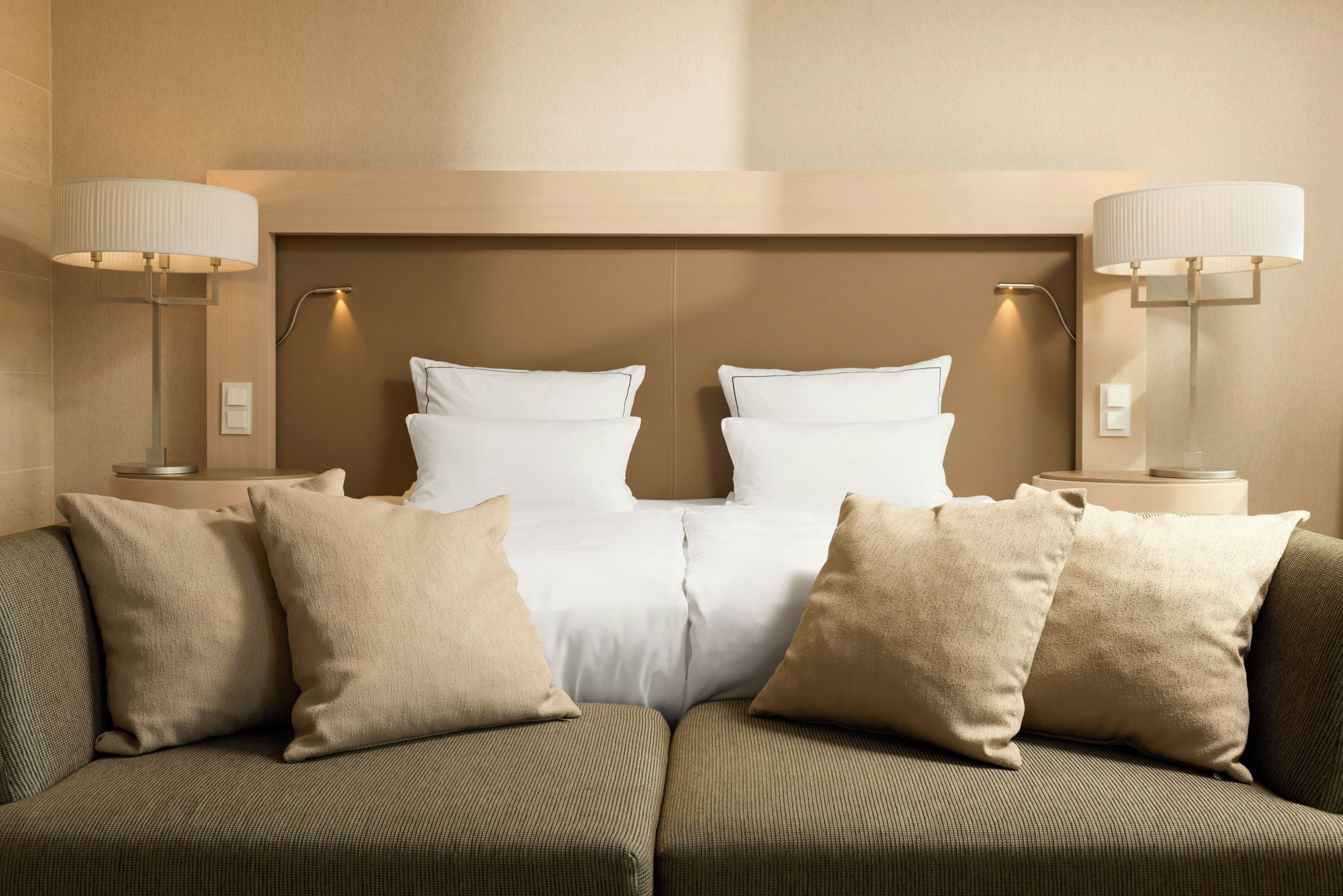 Ein Hotelzimmer mit einem Bett, zwei Nachttischlampen und einem Sofa mit Kissen.