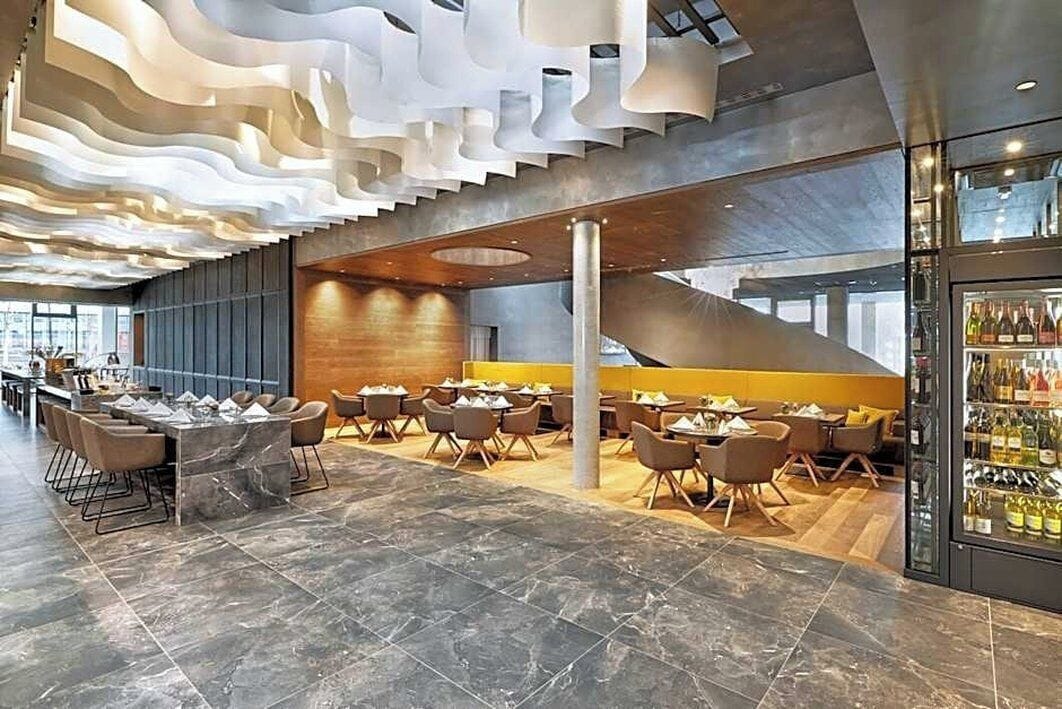 A modern interior with a central seating area, a bar on the right, and a staircase leading to an upper level.