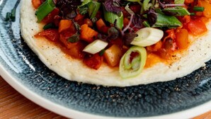 Une assiette de nourriture composée d’une base crémeuse, garnie de légumes coupés en dés et d’herbes fraîches.