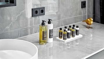 Un mueble de baño con encimera de mármol, un lavabo blanco y una variedad de artículos de aseo, incluyendo botellas y un dispensador de jabón.