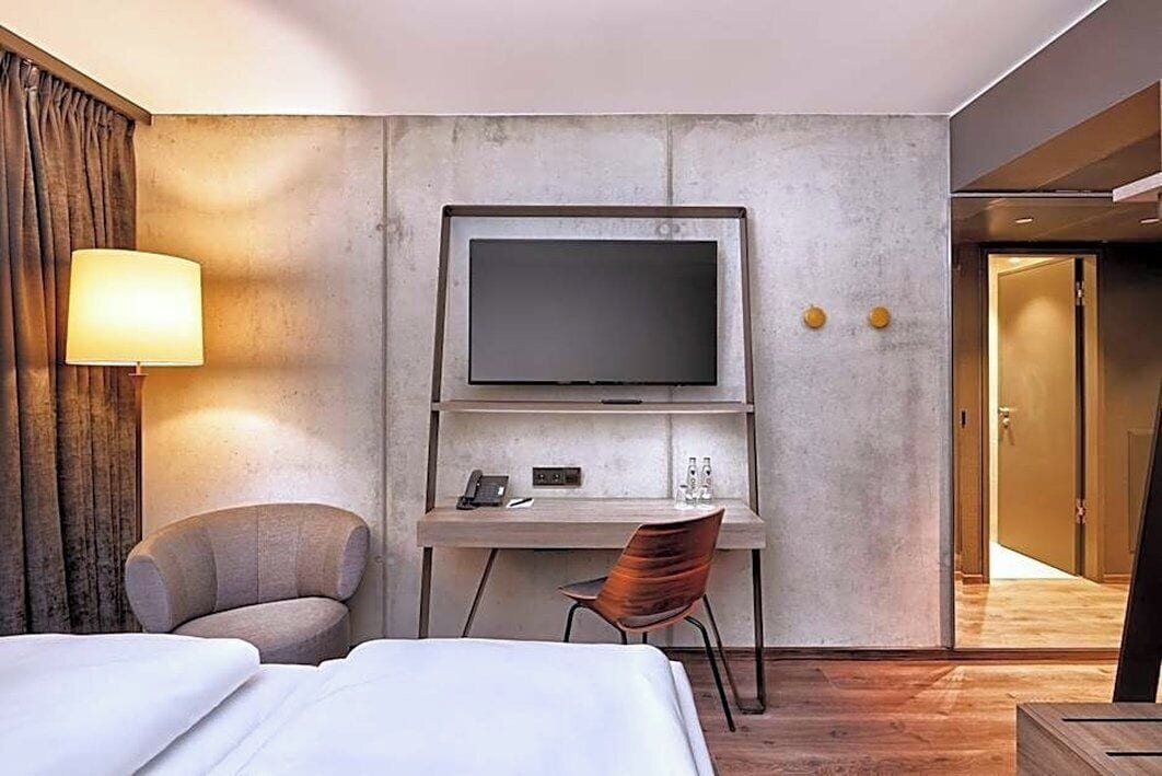 Una habitación de hotel con cama, escritorio, televisor, silla y lámpara.