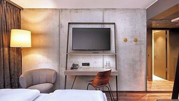 Una habitación de hotel con cama, escritorio, televisor, silla y lámpara.