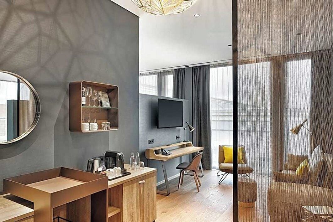 Ein modernes Hotelzimmer mit einem Holztisch, einem Flachbildfernseher, einem Sofa und einem großen Fenster.