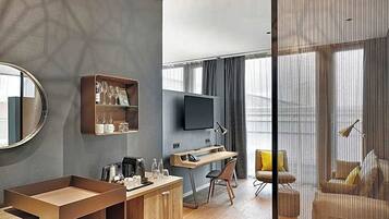 Ein modernes Hotelzimmer mit einem Holztisch, einem Flachbildfernseher, einem Sofa und einem großen Fenster.