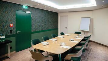 A conference room with a long table, chairs, a whiteboard, and a door with an emergency exit sign.