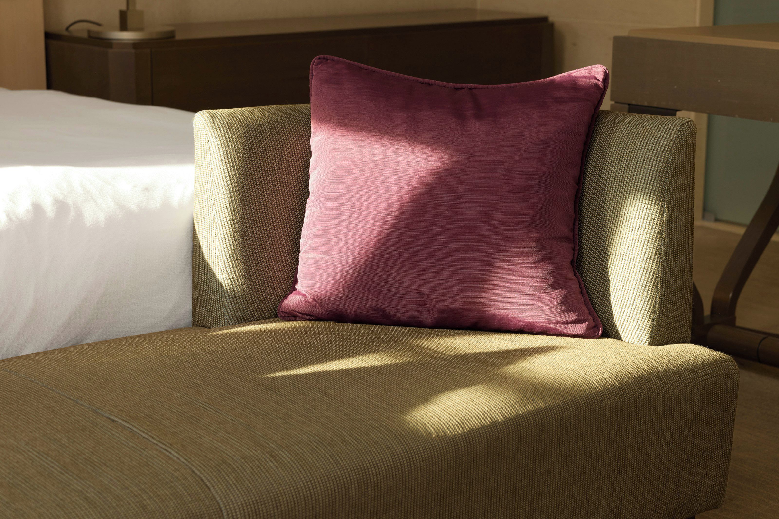 Ein Hotelzimmer mit einem Bett, einem grünen Polsterstuhl und einem einzelnen violetten Kissen.