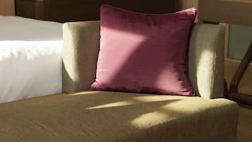 Ein Hotelzimmer mit einem Bett, einem grünen Polsterstuhl und einem einzelnen violetten Kissen.