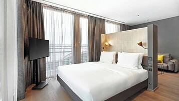 Una camera d'albergo moderna con un ampio letto, una TV a schermo piatto, un divano e vista sulla città.