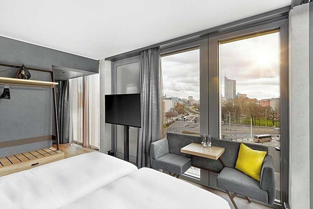 Ein Hotelzimmer mit Bett, Fernseher, kleinem Tisch und einer Couch mit Blick auf die Stadt.