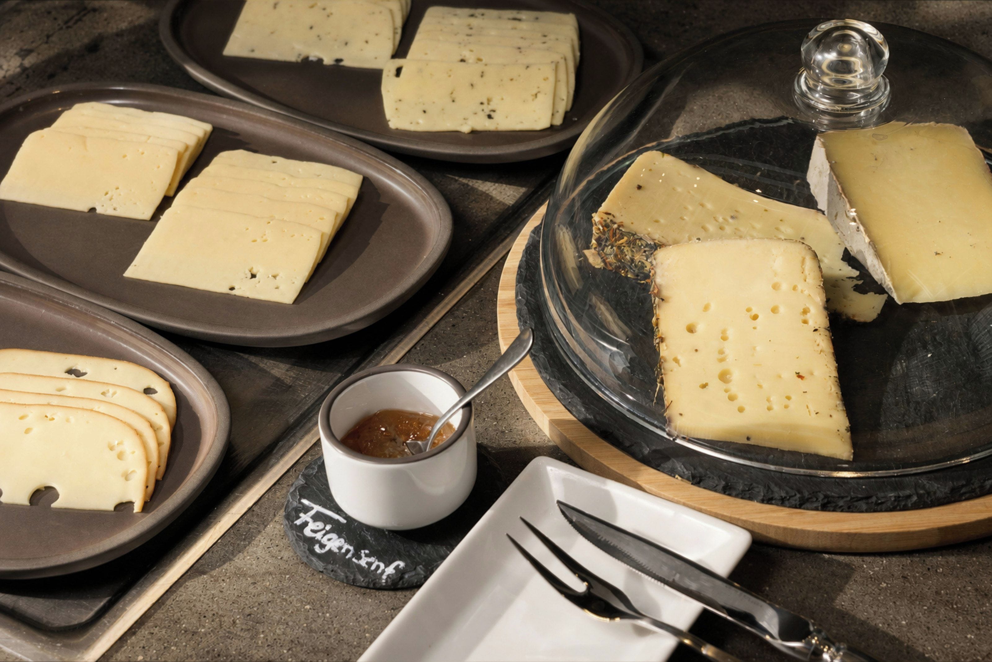 A cheese platter with various types of cheese, a small bowl of jam, and a knife on a table.
