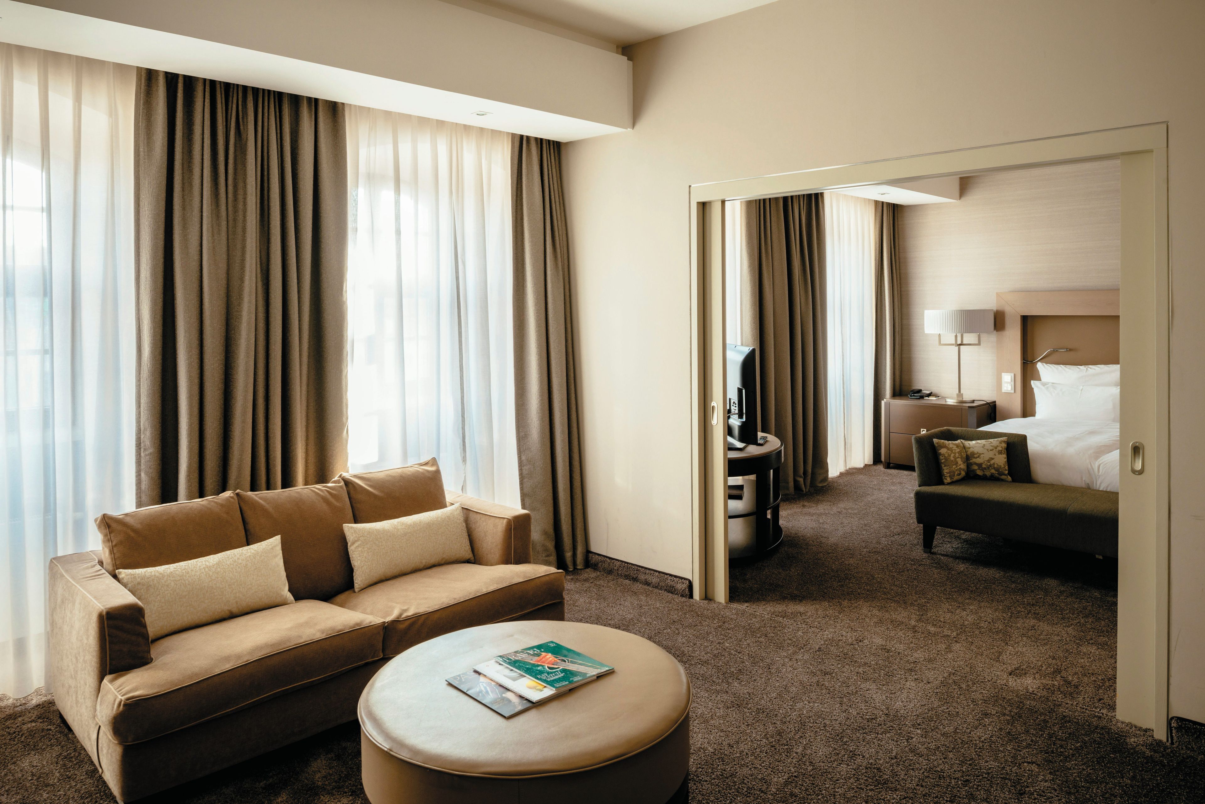 A hotel room with a sofa, ottoman, and a bed.