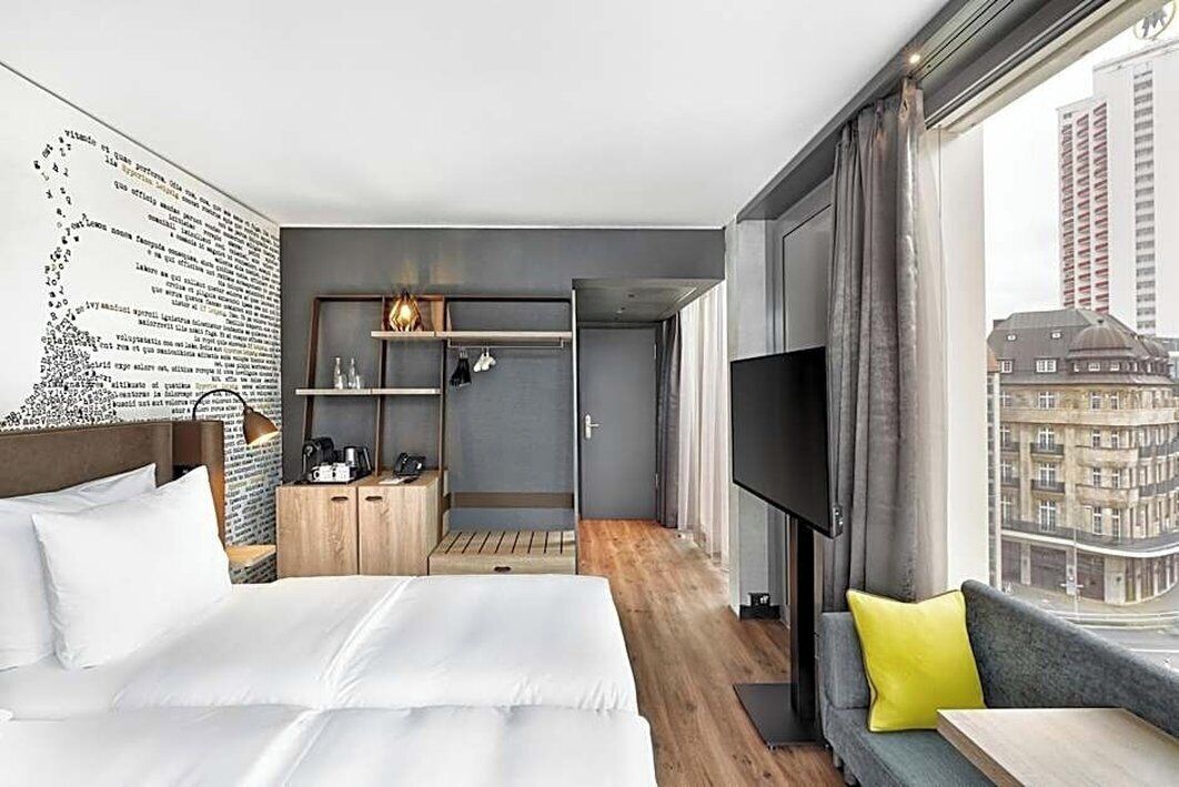 A hotel room with a large bed, a seating area, a TV, and a view of the city.
