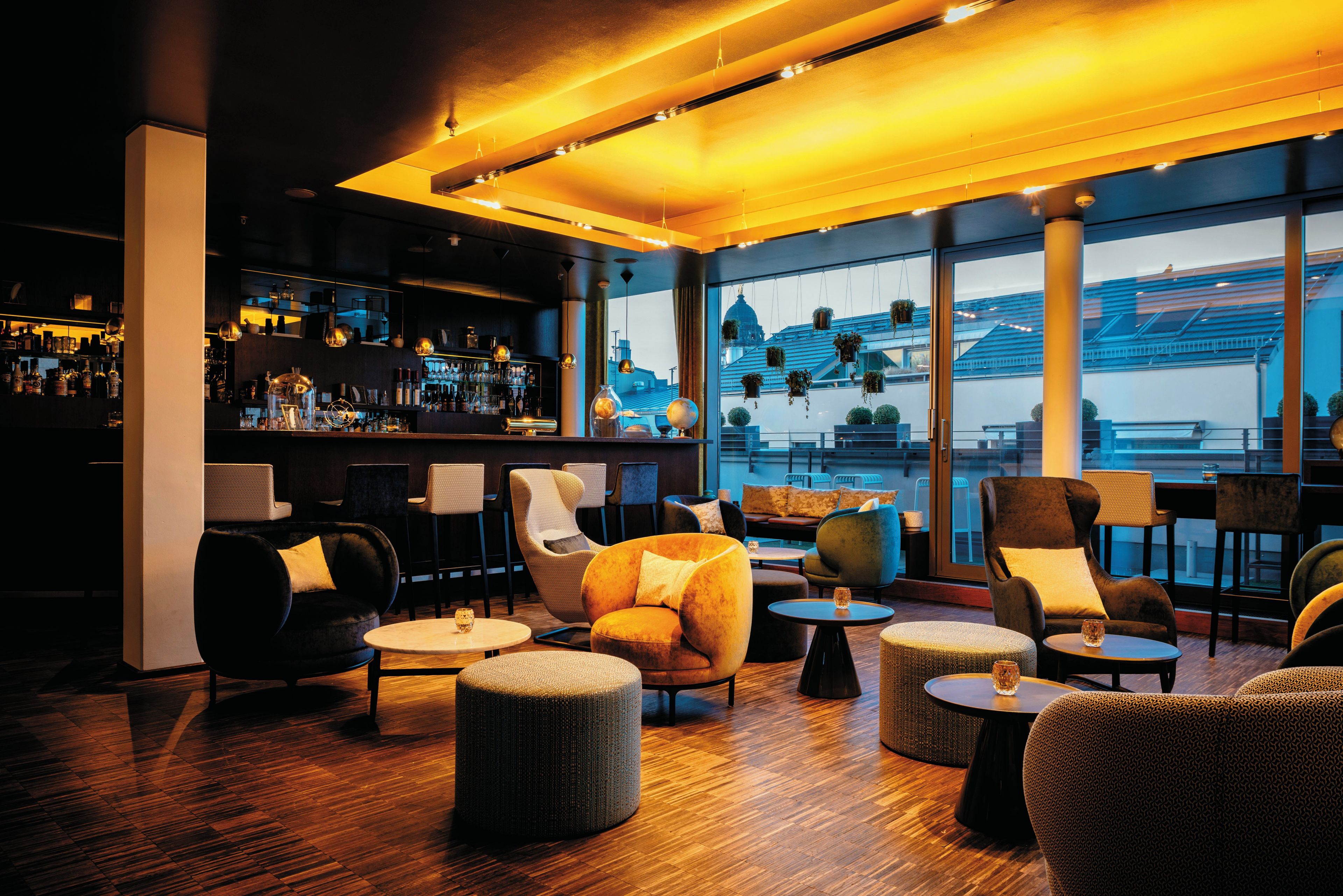 A modern bar area with a city view, featuring a bar counter, seating, and a large window.