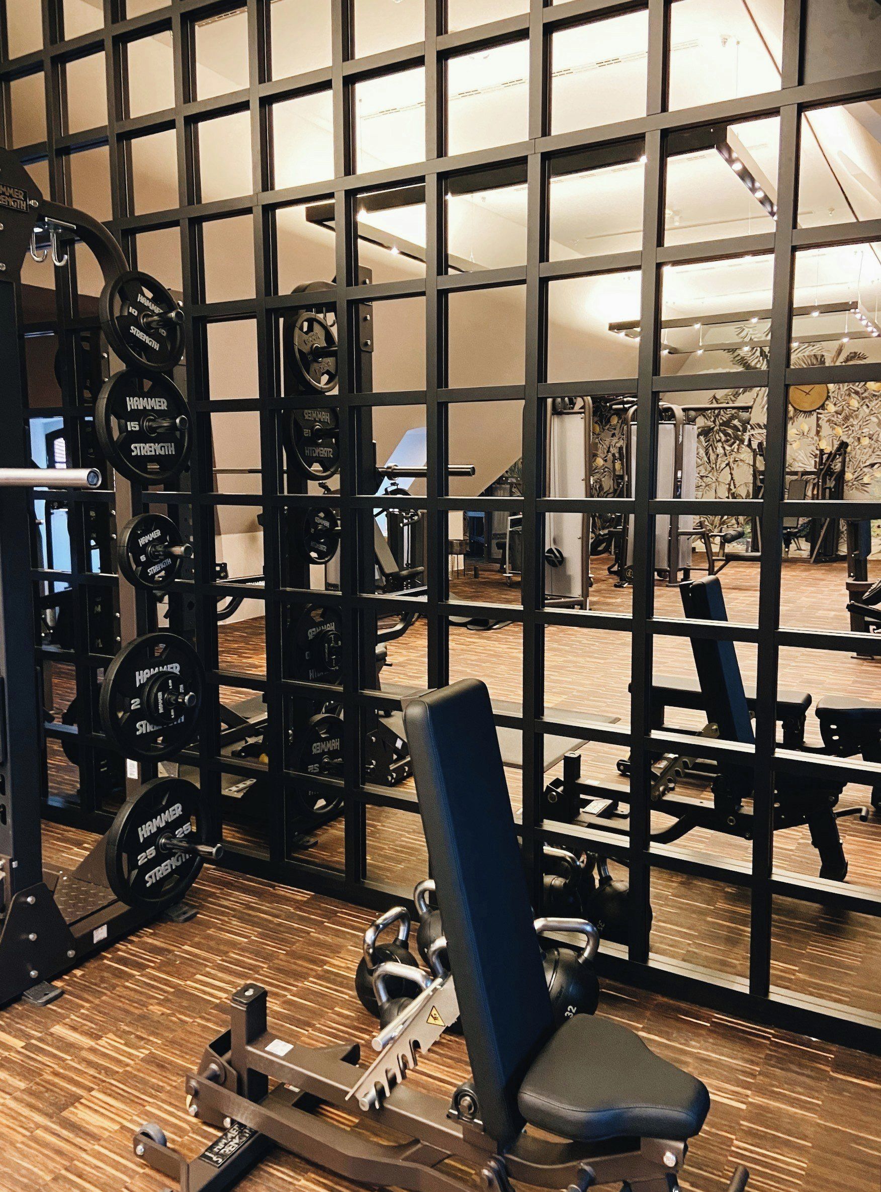 A gym with weightlifting equipment, a bench, and a mirror reflecting the interior.