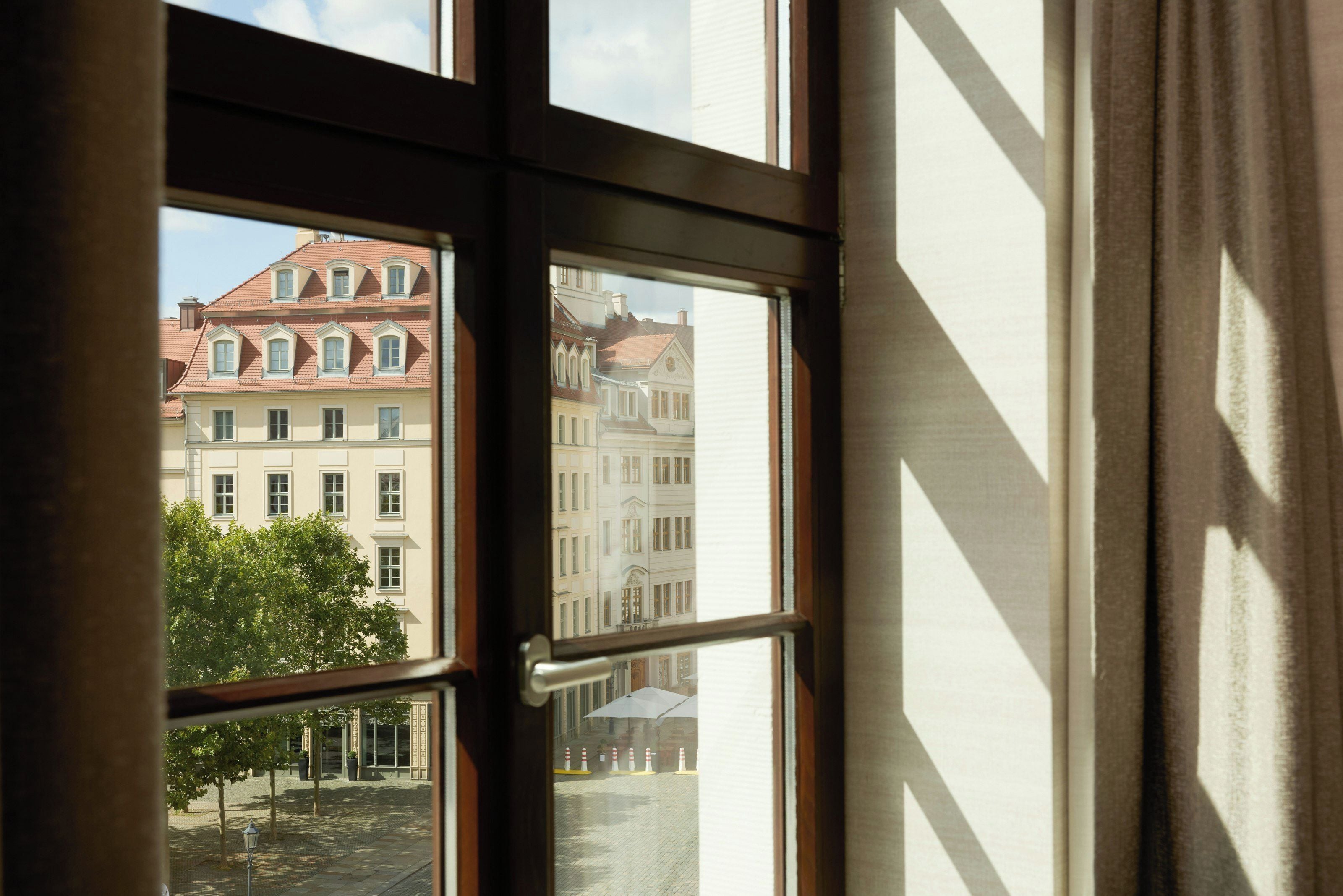Une vue à travers une fenêtre, donnant sur des immeubles et un arbre.