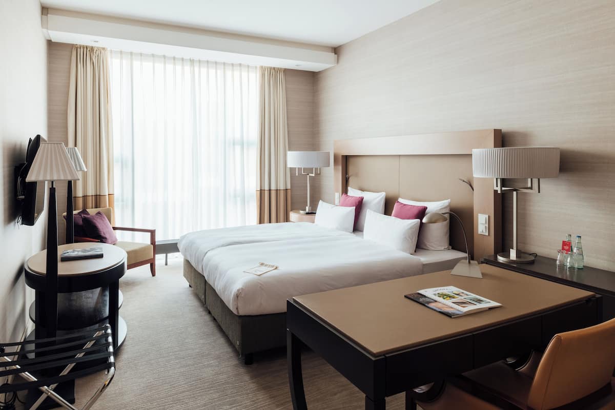 Ein Hotelzimmer mit einem großen Bett, zwei Nachttischen, einem Schreibtisch, einem Stuhl und einem an der Wand befestigten Fernseher.