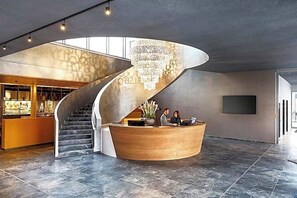 A modern reception area with a curved staircase, a chandelier, and a reception desk. - The Cloud One Dresden-Frauenkirche (Dresden)