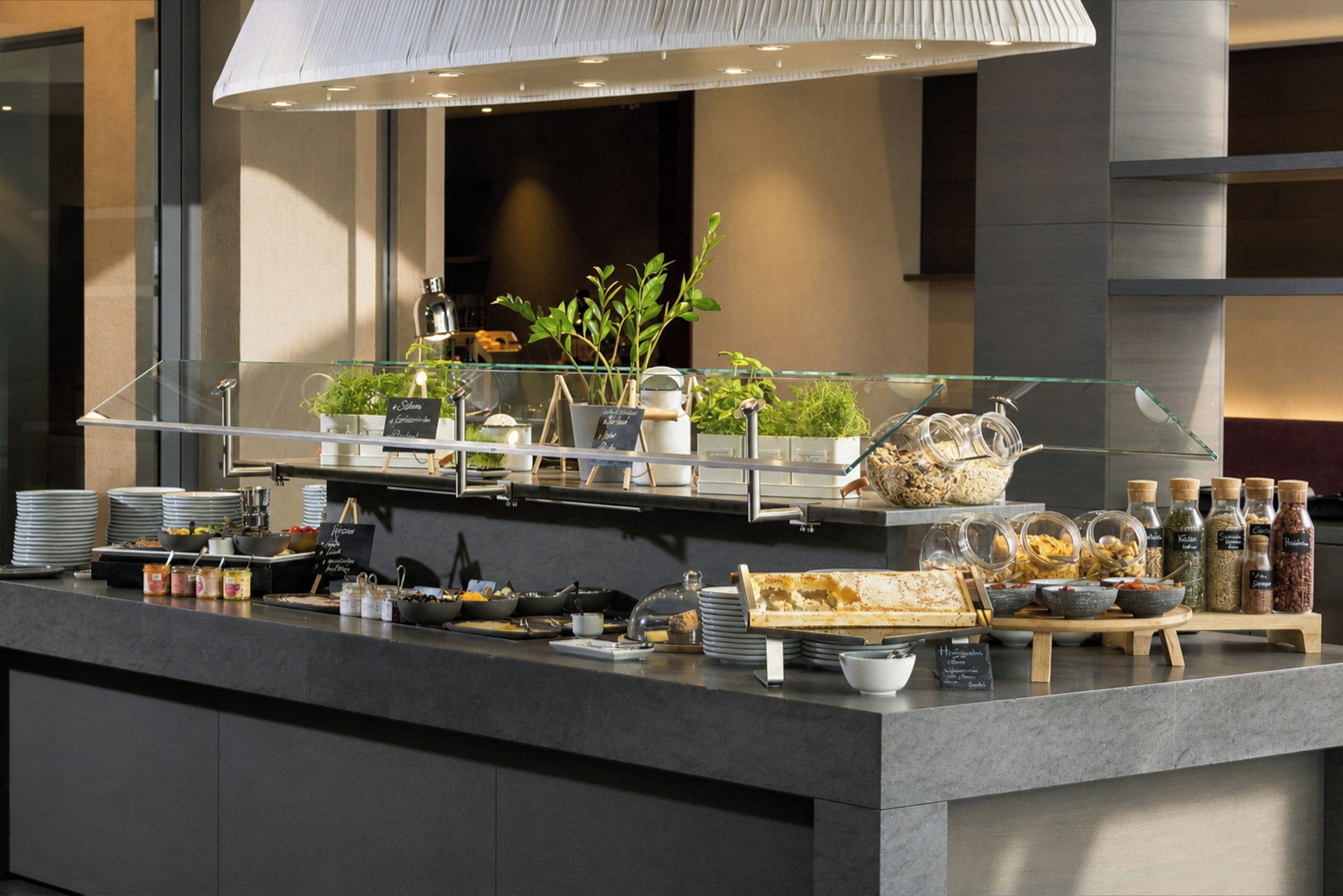 Montaje de bufé con diversos alimentos, un expositor de vidrio y una decoración interior moderna.