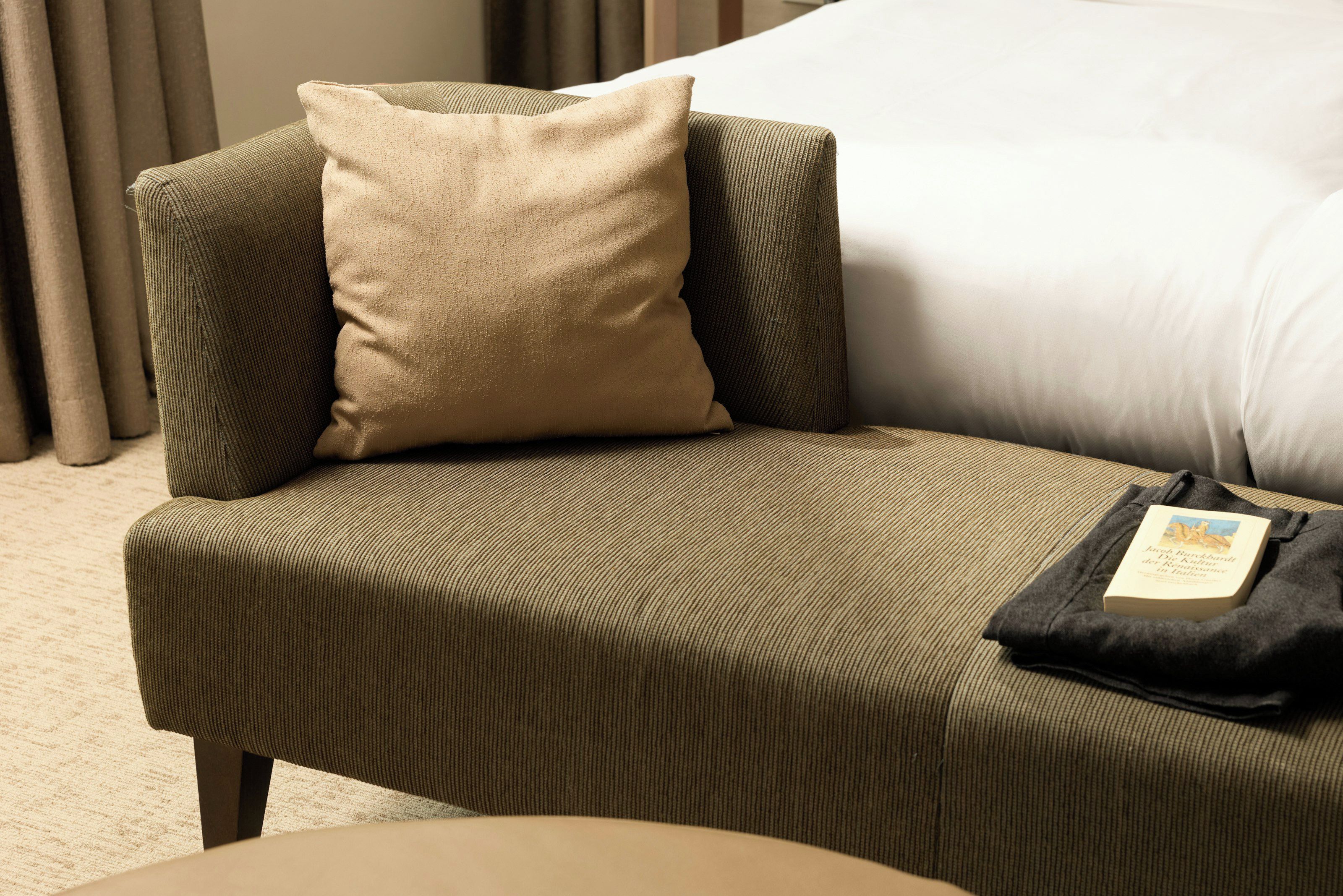 A corner sofa with a cushion and a black bag on it.