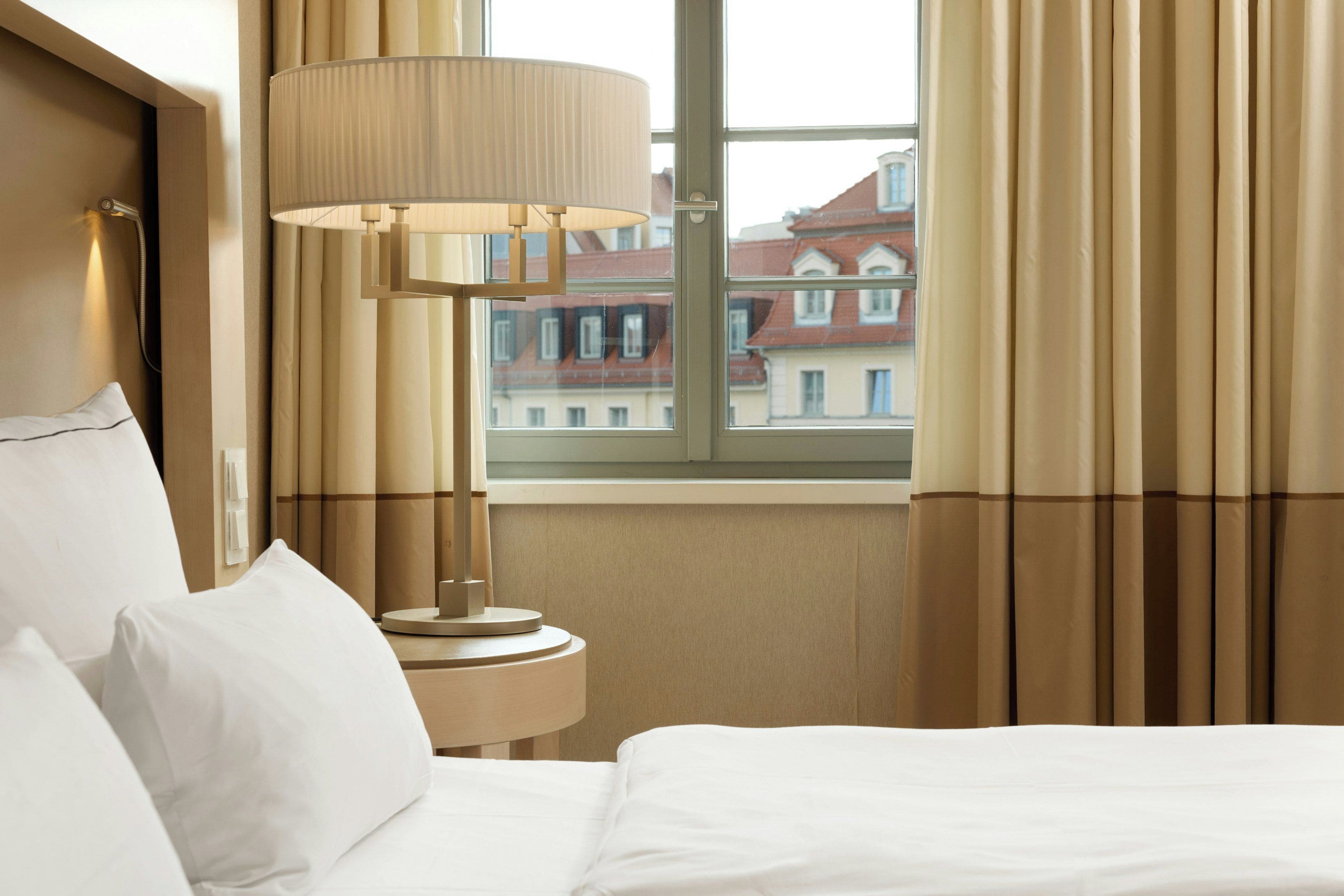 A hotel room with a bed, a lamp, and a window with curtains.