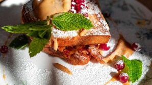 Un dessert présenté dans une assiette, saupoudré de sucre glace, garni de feuilles de menthe et de fruits rouges.