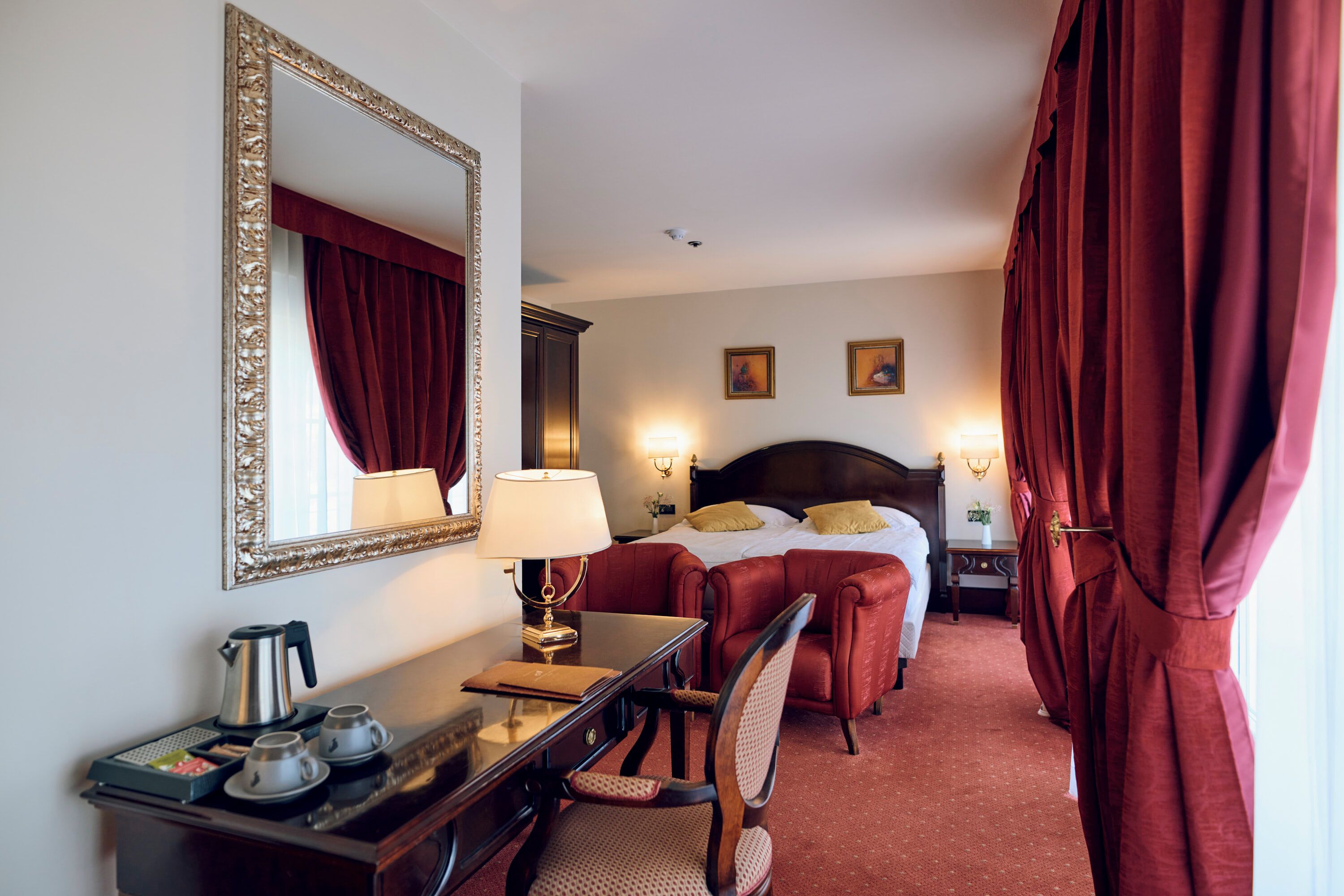 A hotel room with a large bed, a desk with a lamp, a chair, and a mirror.