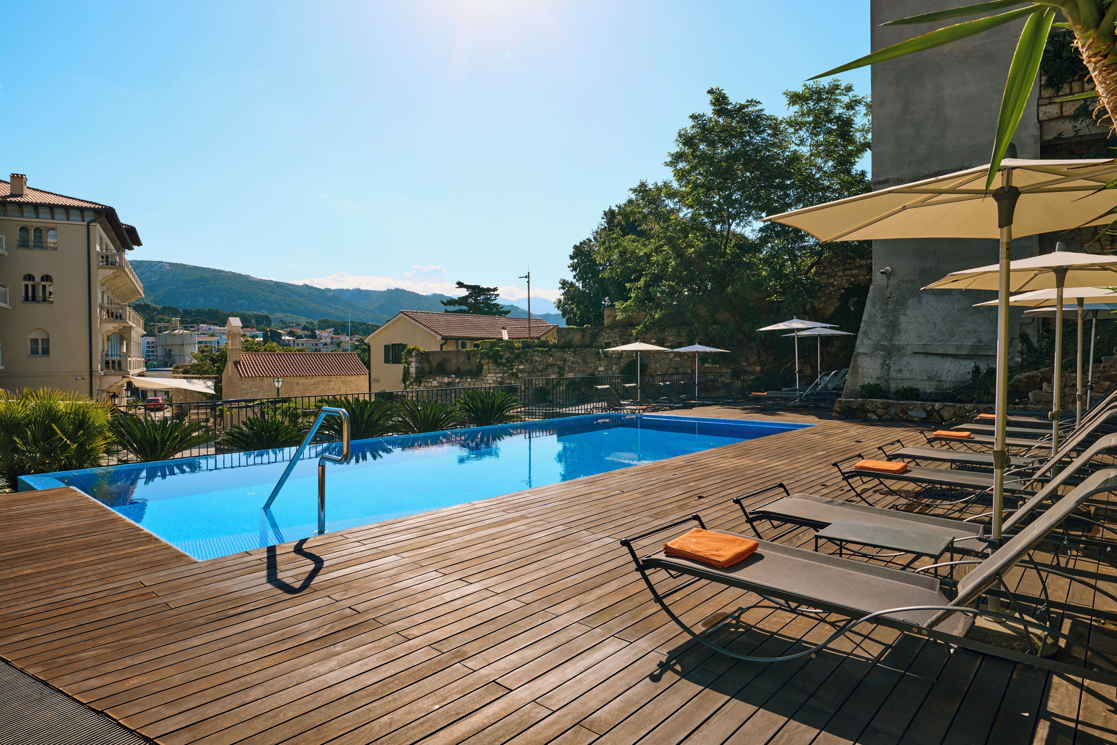 Una terrassa de fusta amb piscina, gandules i ombrel·les.
