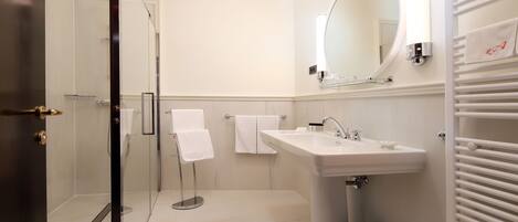 A modern bathroom with a glass shower enclosure, a pedestal sink, and a large mirror above the sink.