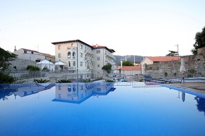 A swimming pool with clear water, surrounded by buildings and a stone wall. - Arbiana Heritage Hotel (Rab)
