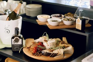 Una tabla de embutidos con varios quesos, frutos secos y frutas, junto con una botella de aceite de oliva y una botella de champán.