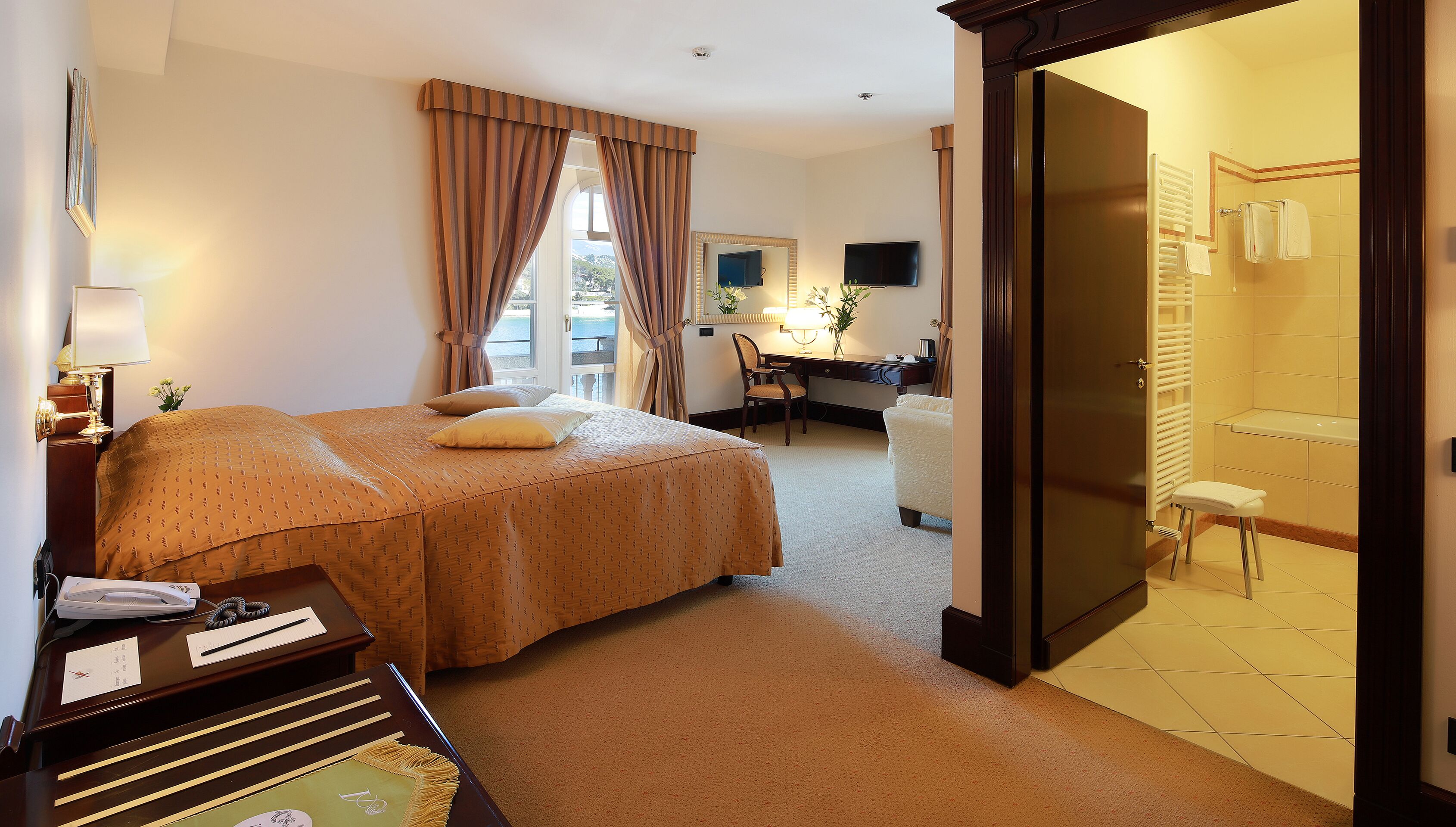 A hotel room with a bed, desk, chair, and a bathroom visible through an open door.