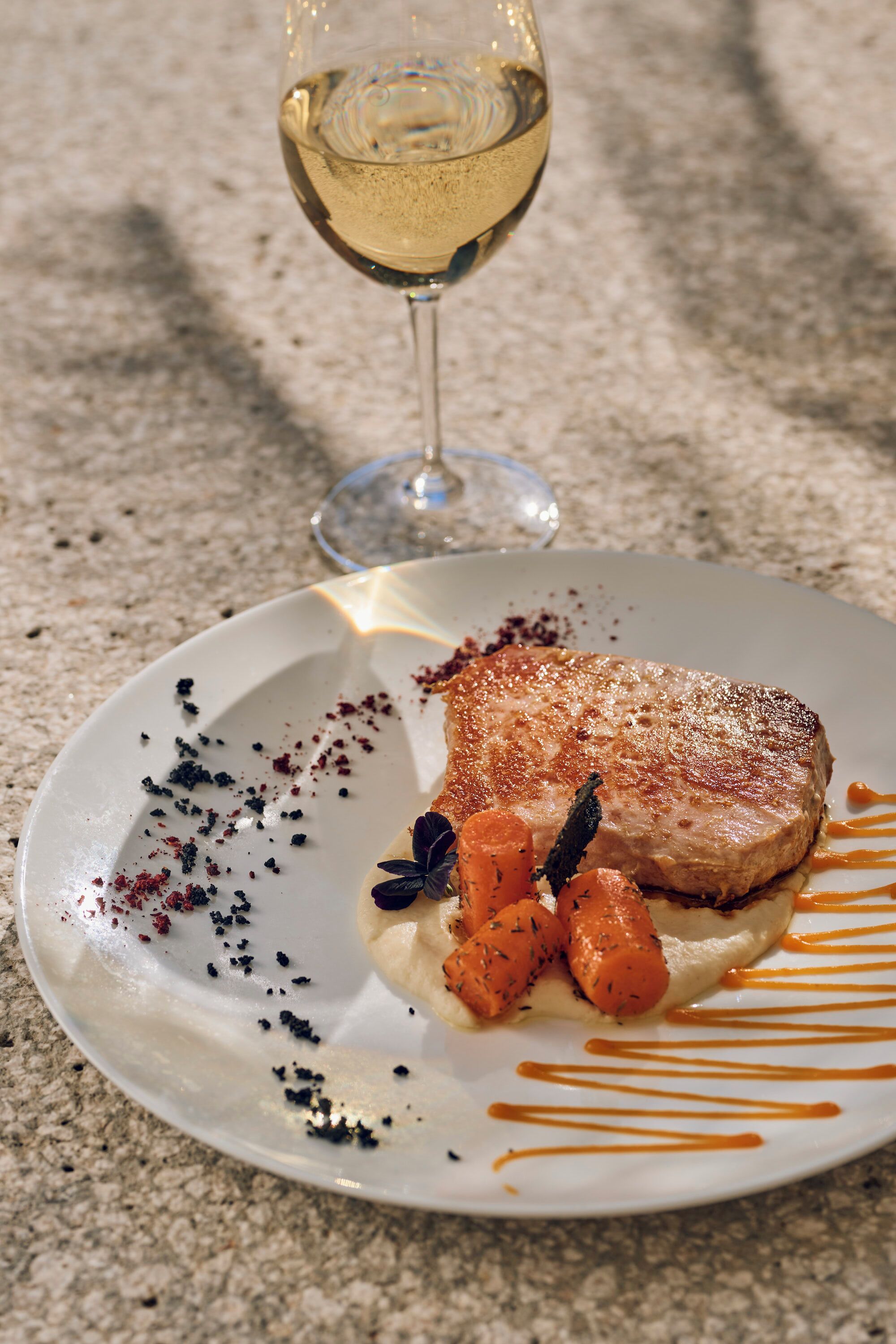 A plate with a steak, carrots, and sauce on a textured surface.