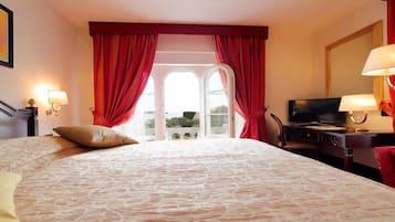 Habitación de hotel con una cama grande, un escritorio con televisor y un balcón con cortinas rojas.