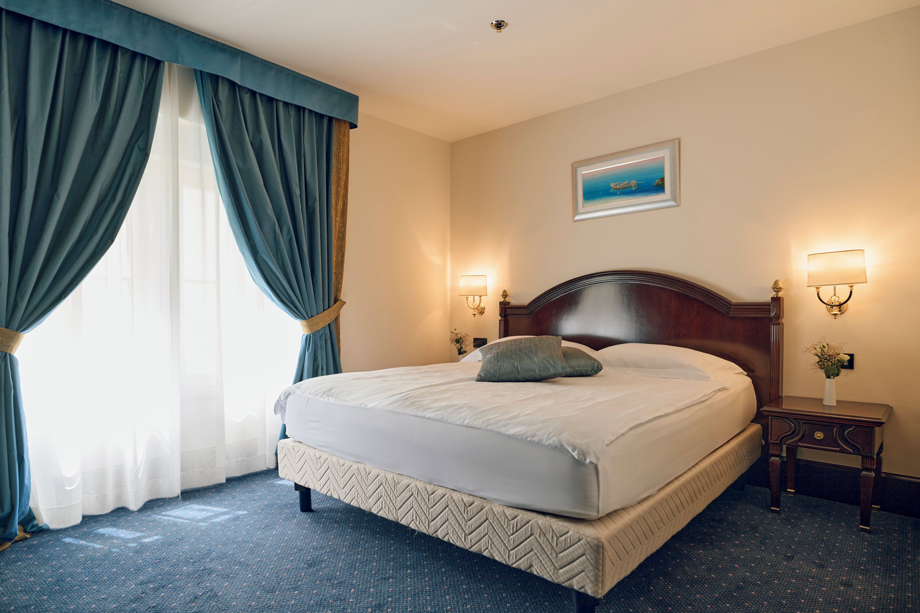 A hotel room with a large bed, two bedside lamps, a nightstand, and a painting on the wall.