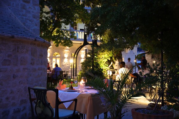 An outdoor dining area with tables set for two, surrounded by stone walls and potted plants. - Arbiana Heritage Hotel (Rab)