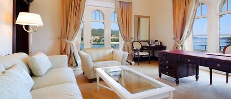 Une chambre d’hôtel équipée d’un canapé, d’un fauteuil, d’un bureau et offrant une vue sur la mer.