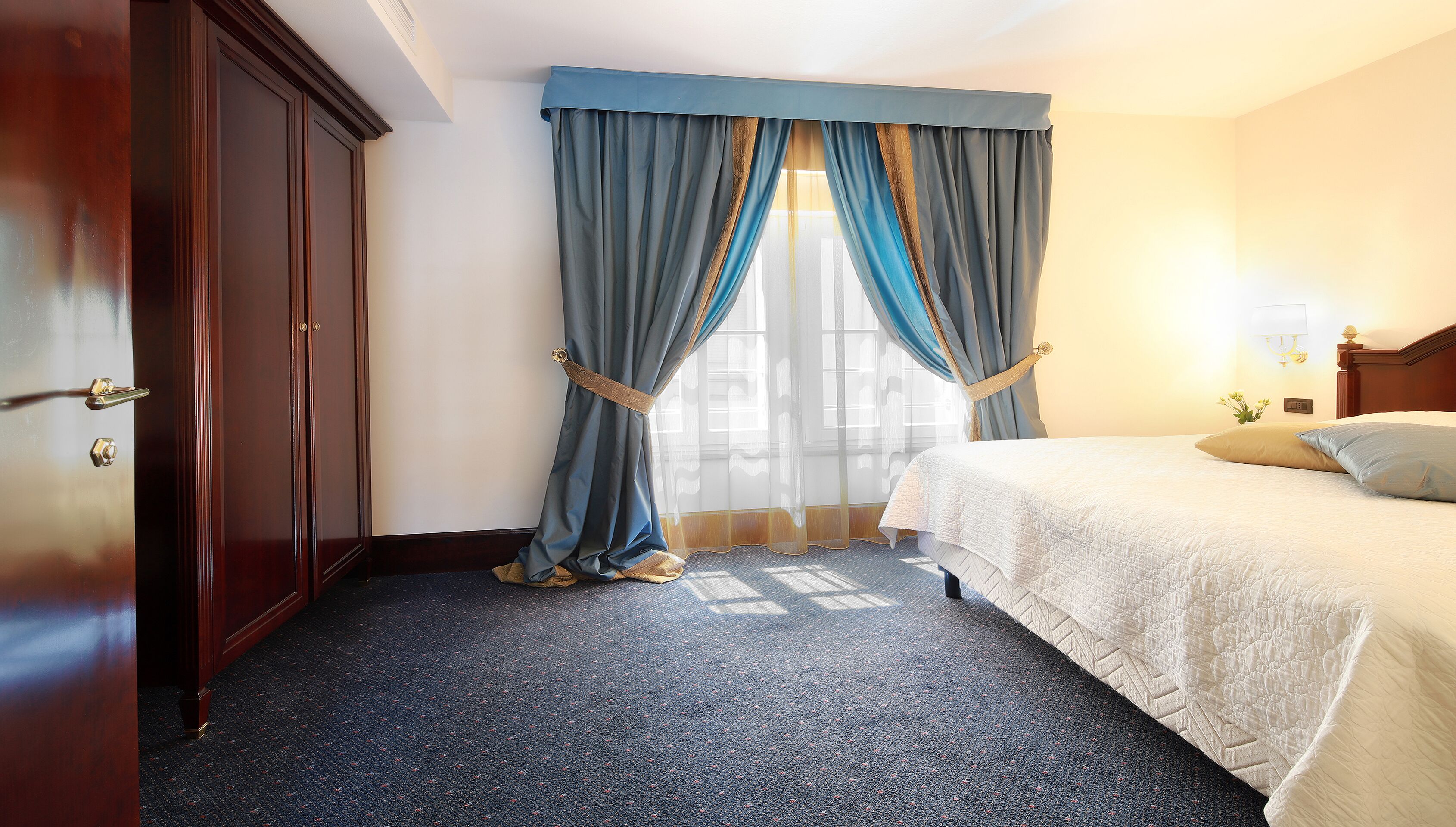 A hotel room with a bed, a wardrobe, and a window with curtains.